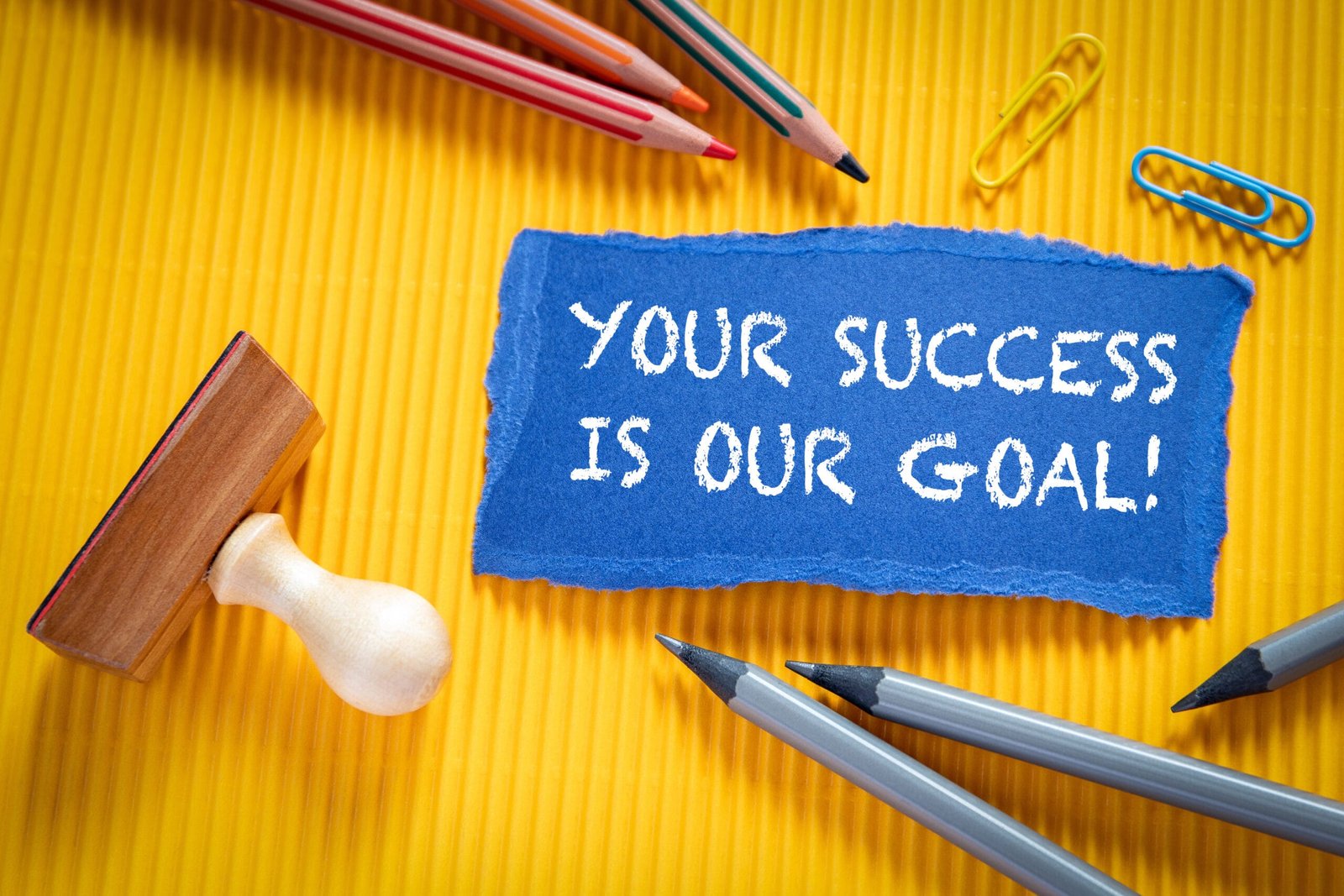 YOUR SUCCESS IS OUR GOAL. Text on torn, colored paper